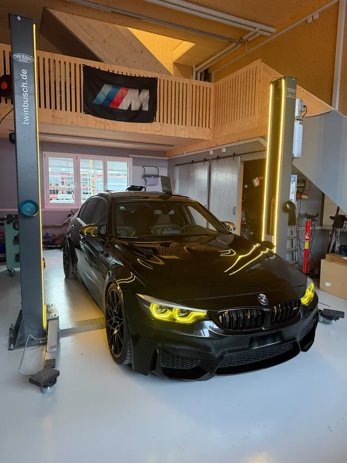 Schwarzer BMW M3 mit gelbem Tagfahrlicht zwischen beleuchteten Hebebühnen