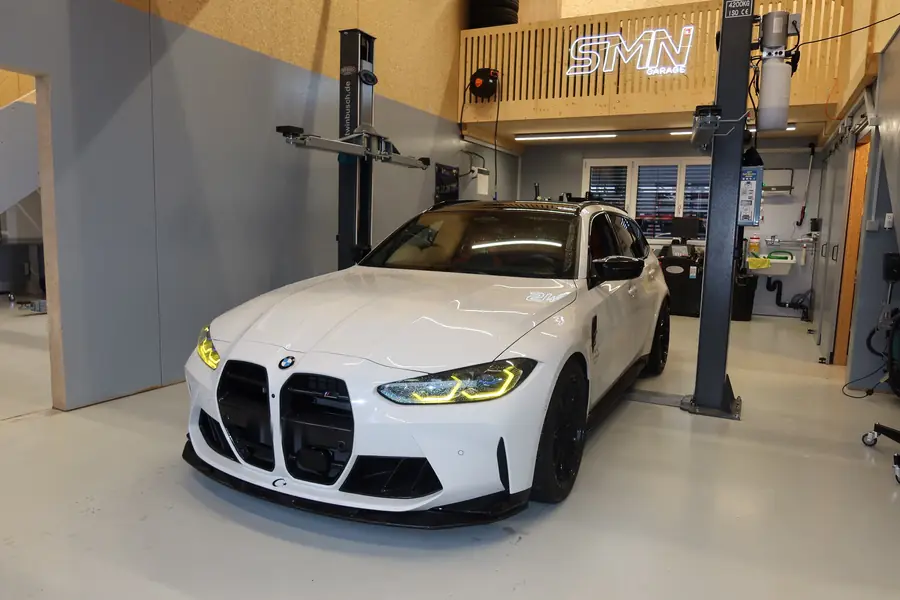 Weisser BMW M3 Touring vor dem SMN-Neonlogo
